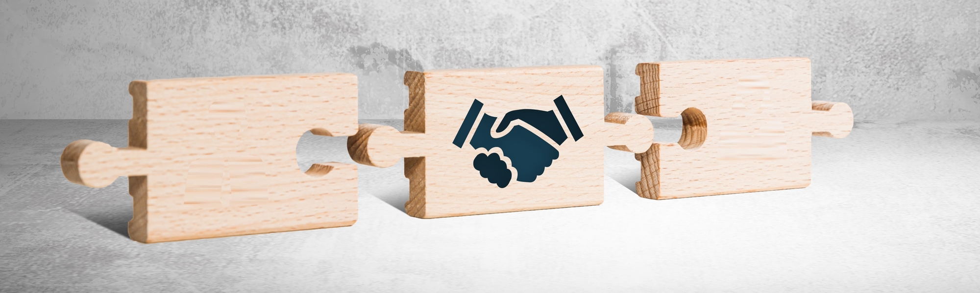 Drei Puzzlestücke, das mittlere hat ein Handschlag Icon darauf.